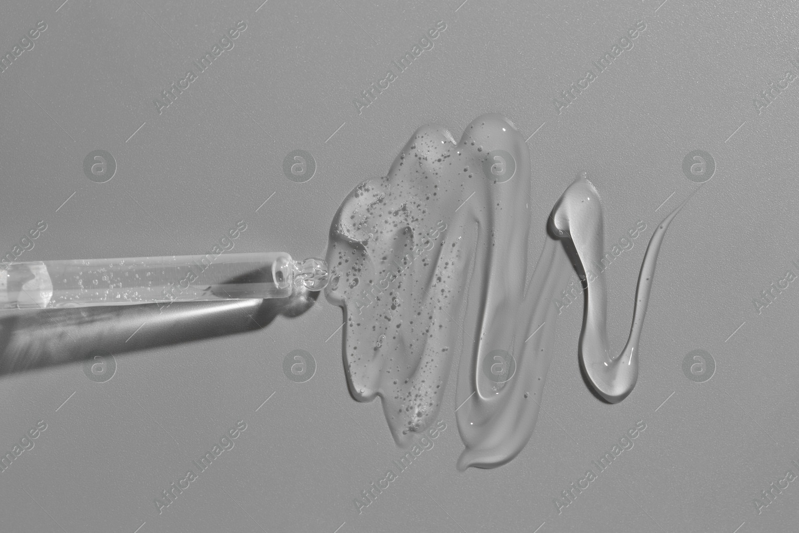 Photo of Dripping cosmetic serum from pipette on grey background, top view