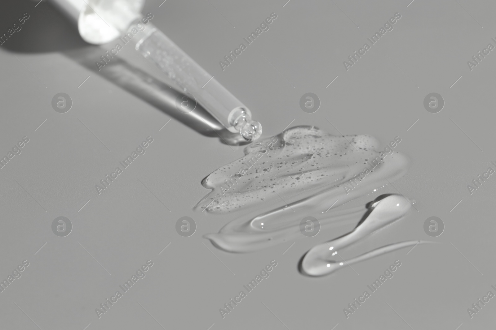 Photo of Dripping cosmetic serum from pipette on grey background, closeup