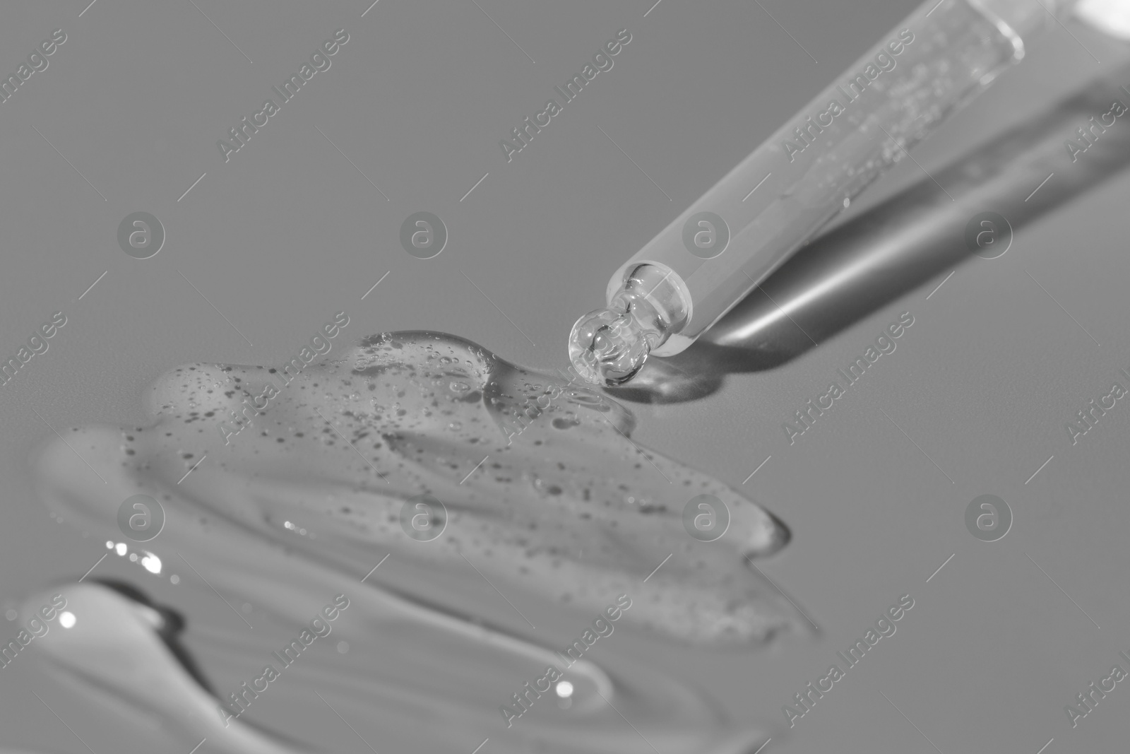 Photo of Dripping cosmetic serum from pipette on grey background, closeup