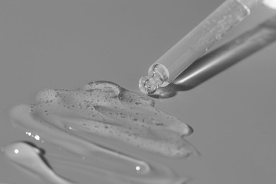 Dripping cosmetic serum from pipette on grey background, closeup