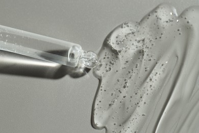 Photo of Dripping cosmetic serum from pipette on grey background, top view