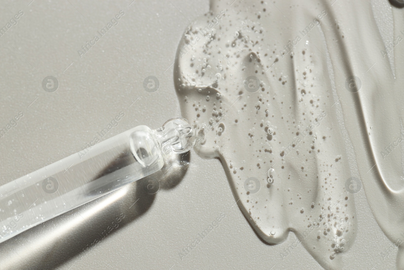 Photo of Dripping cosmetic serum from pipette on grey background, top view