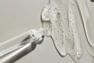 Dripping cosmetic serum from pipette on grey background, top view