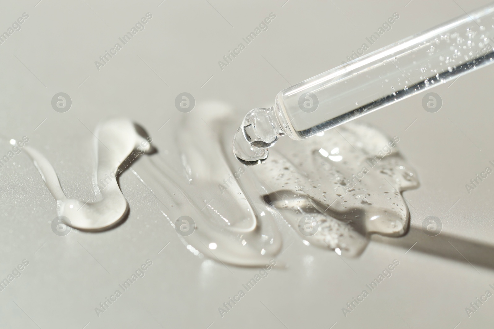 Photo of Dripping cosmetic serum from pipette on grey background, closeup