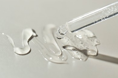 Dripping cosmetic serum from pipette on grey background, closeup