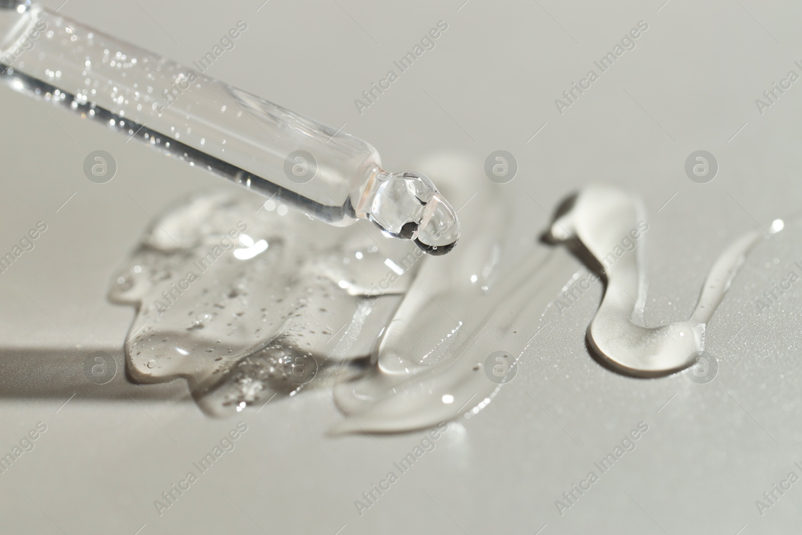 Photo of Dripping cosmetic serum from pipette on grey background, closeup