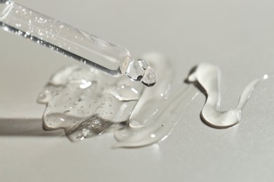 Photo of Dripping cosmetic serum from pipette on grey background, closeup