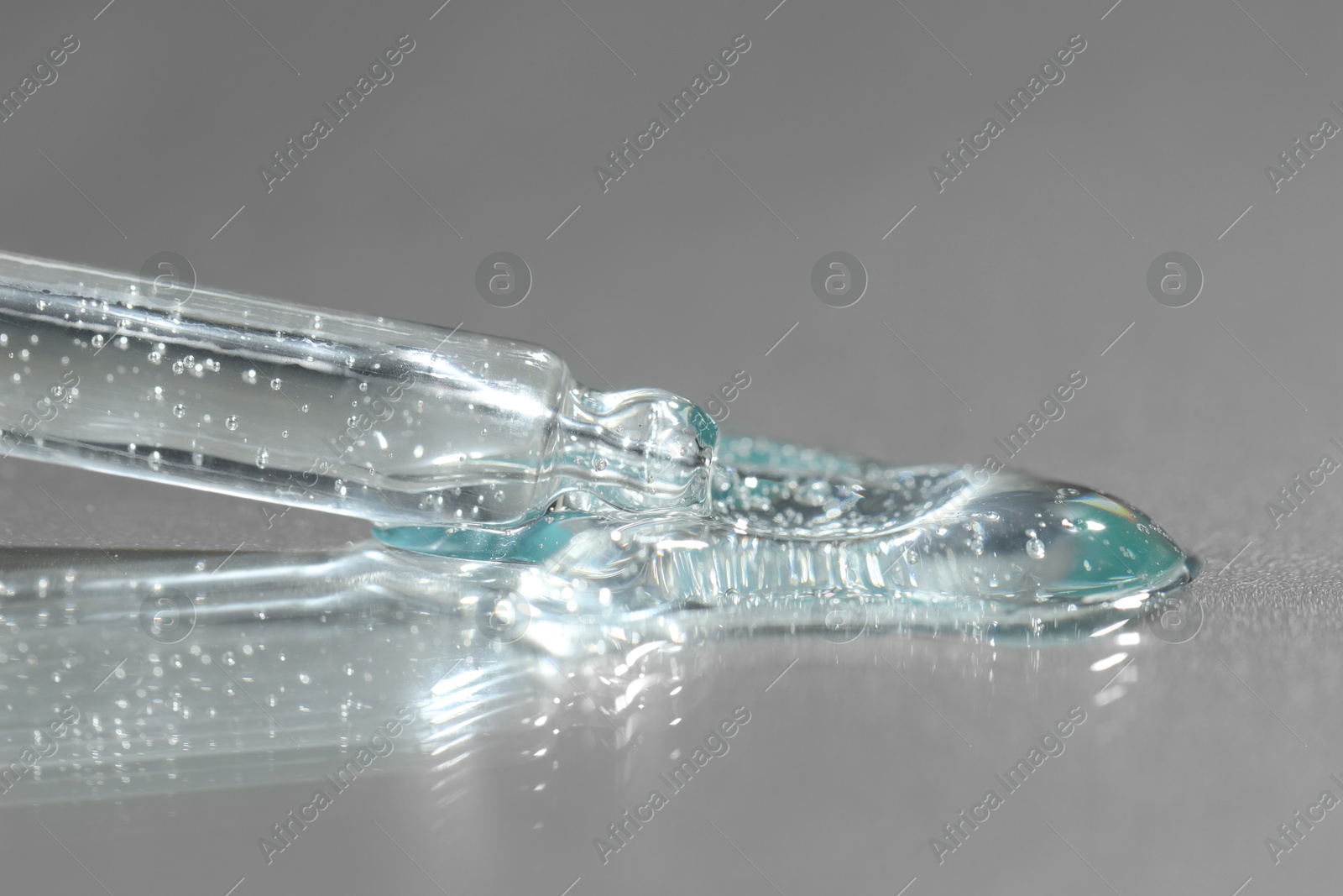 Photo of Dripping cosmetic serum from pipette on grey background, closeup