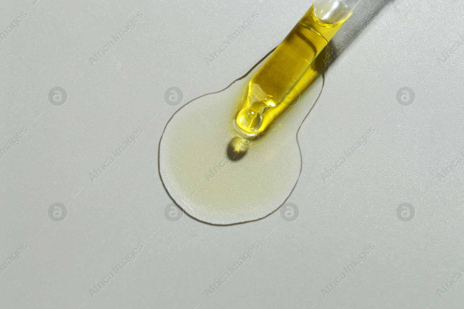 Photo of Dripping essential oil from pipette on grey background, top view