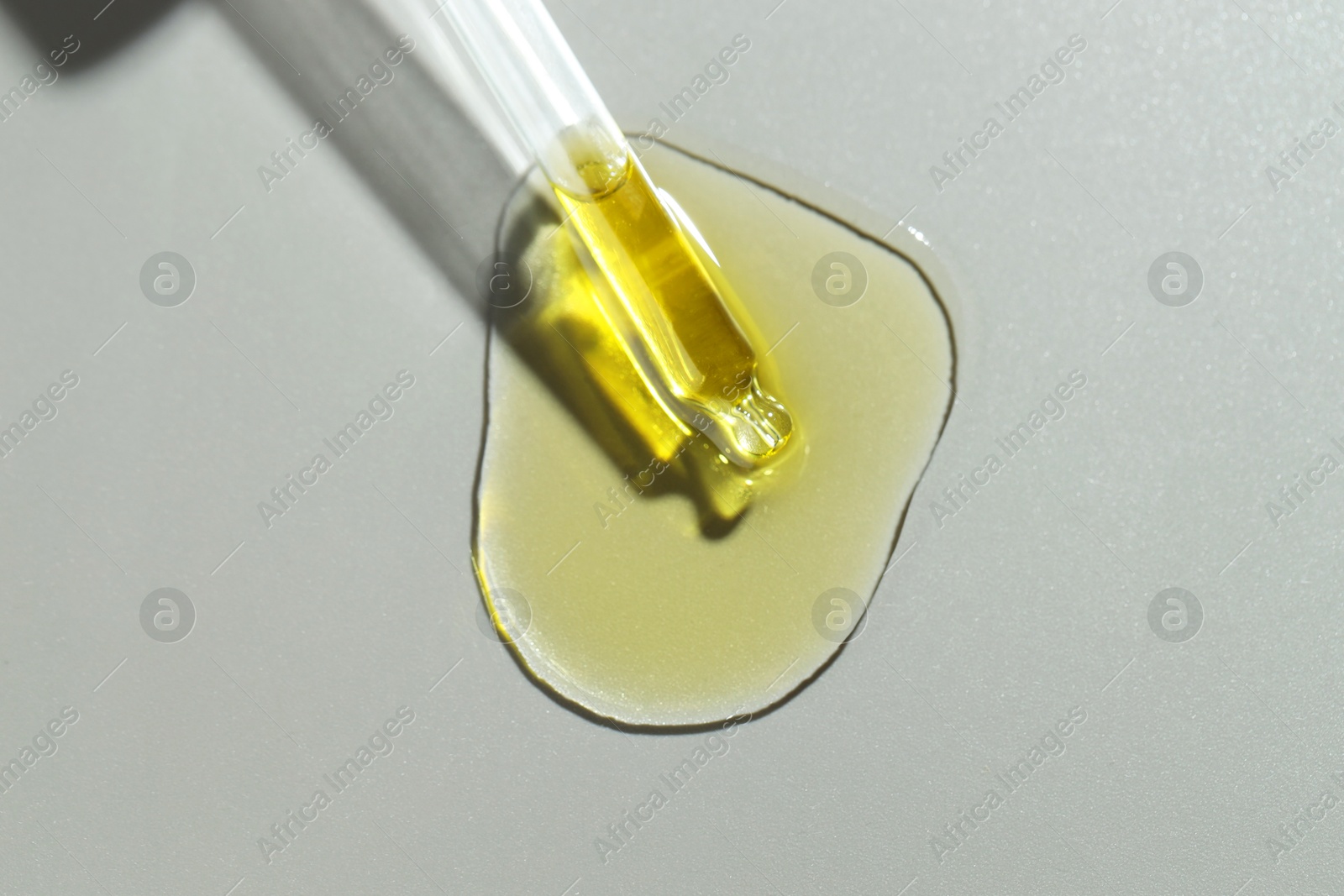 Photo of Dripping essential oil from pipette on grey background, top view