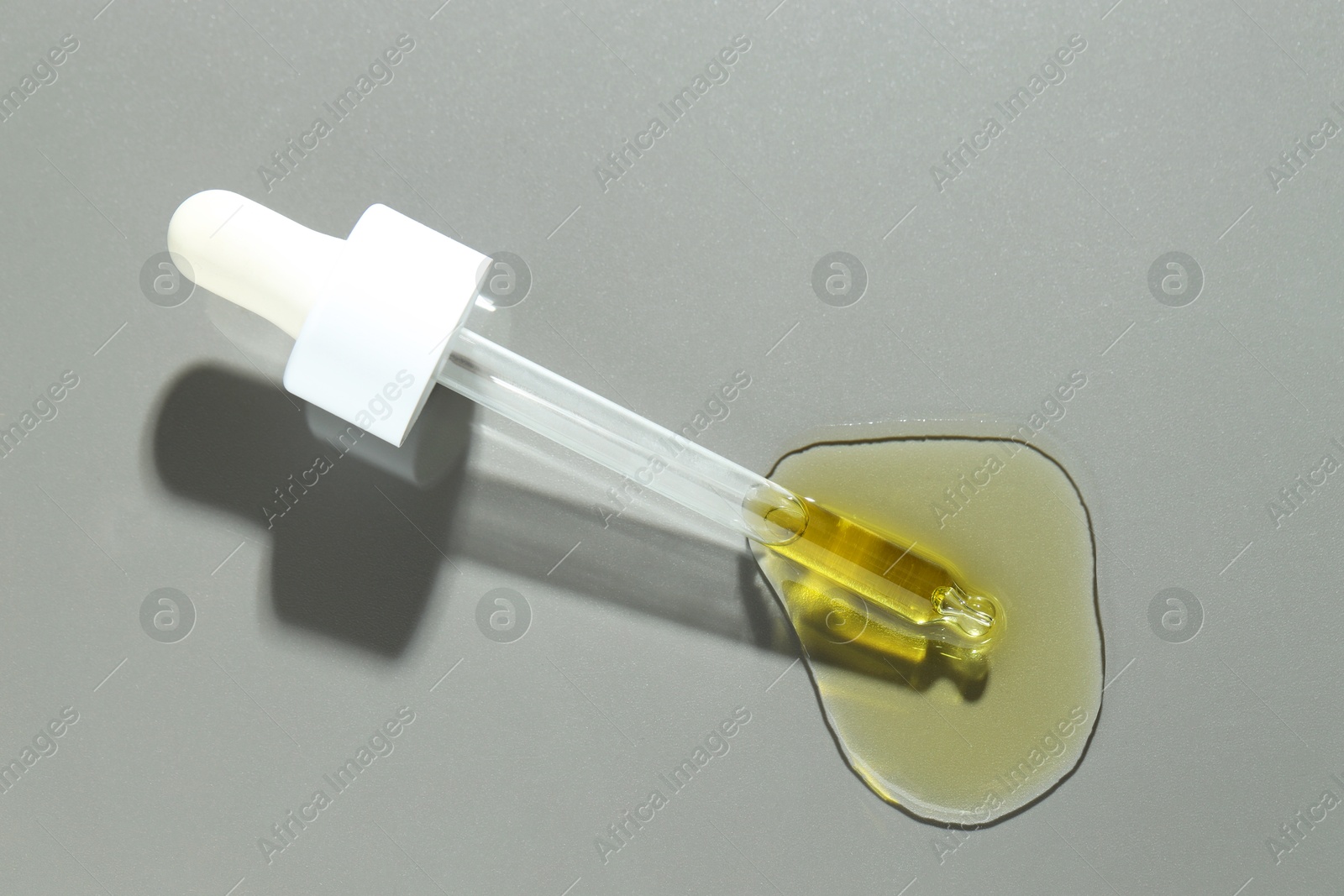 Photo of Dripping essential oil from pipette on grey background, top view