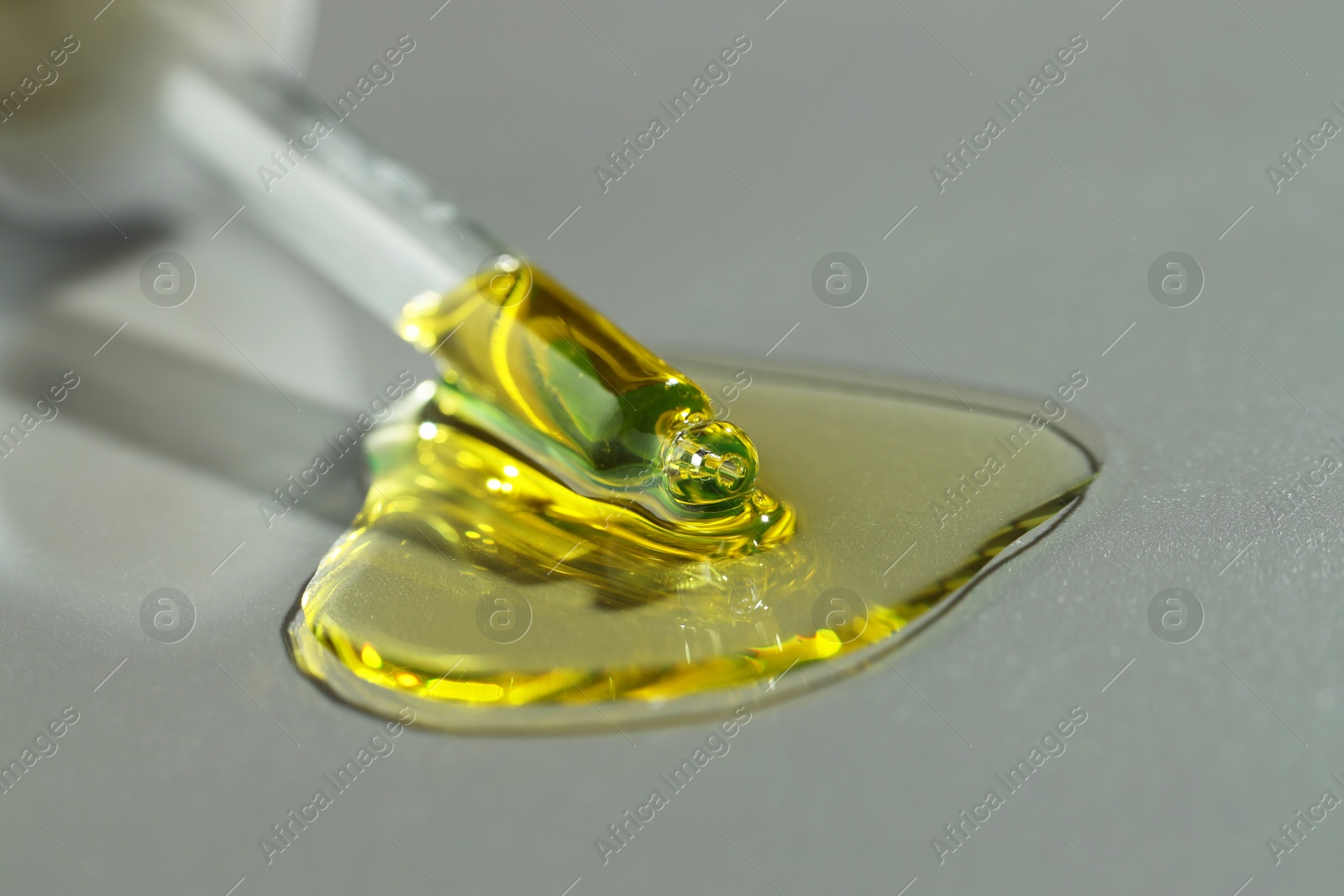 Photo of Dripping essential oil from pipette on grey background, closeup