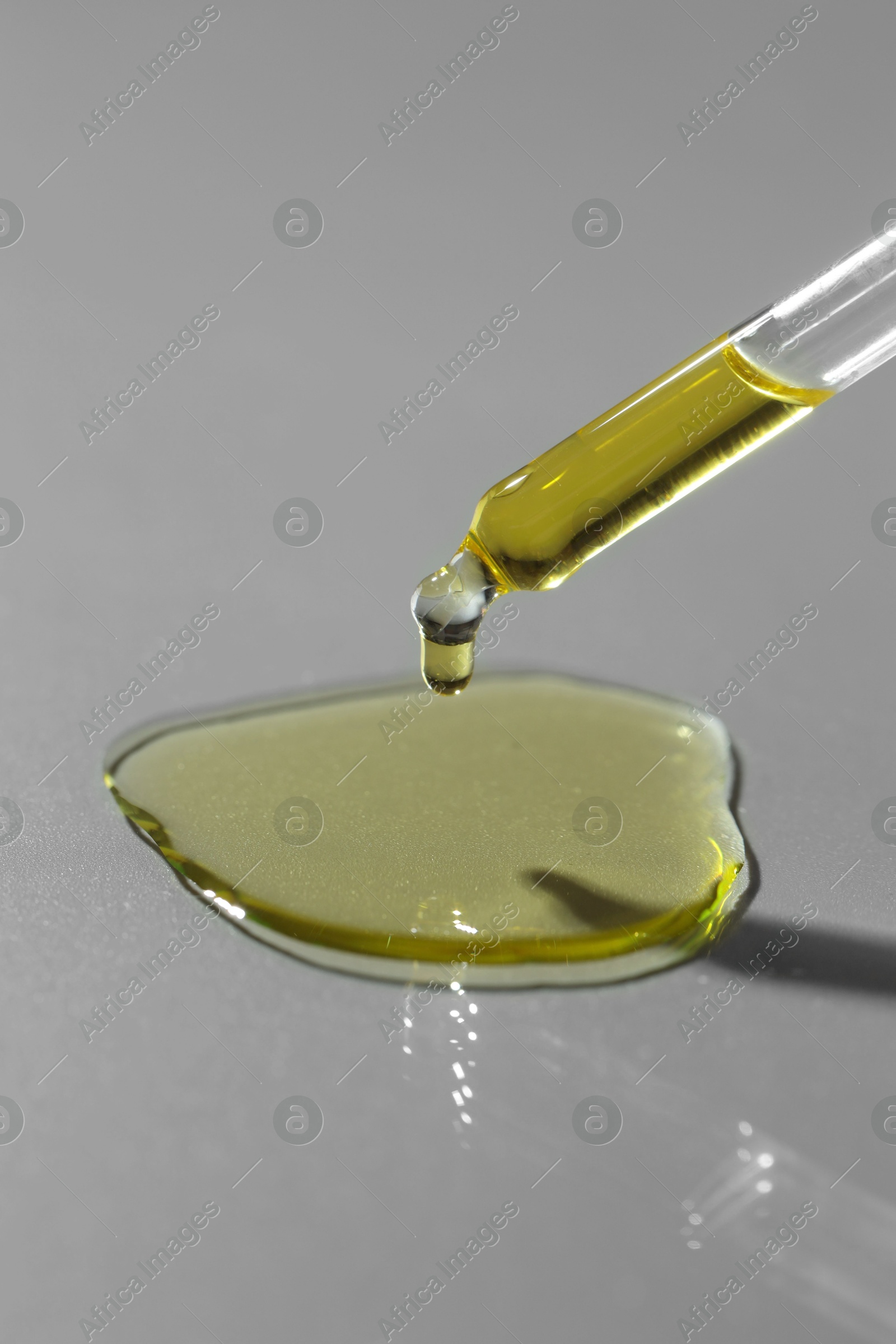 Photo of Dripping essential oil from pipette on grey background, closeup