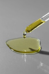 Photo of Dripping essential oil from pipette on grey background, closeup