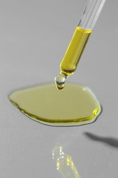 Dripping essential oil from pipette on grey background, closeup