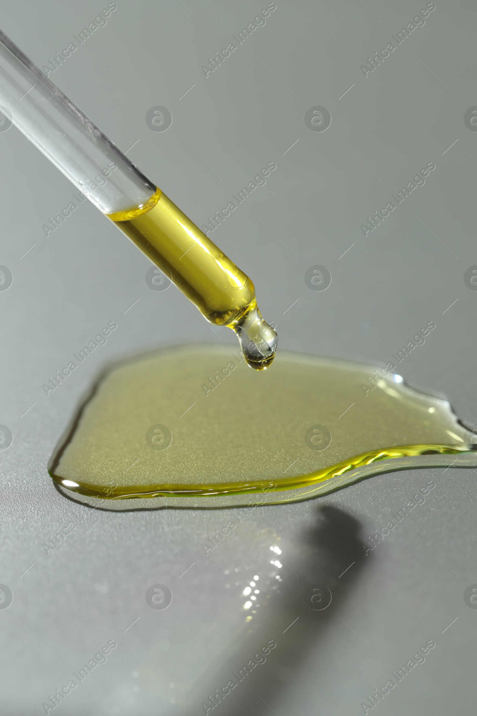 Photo of Dripping essential oil from pipette on grey background, closeup