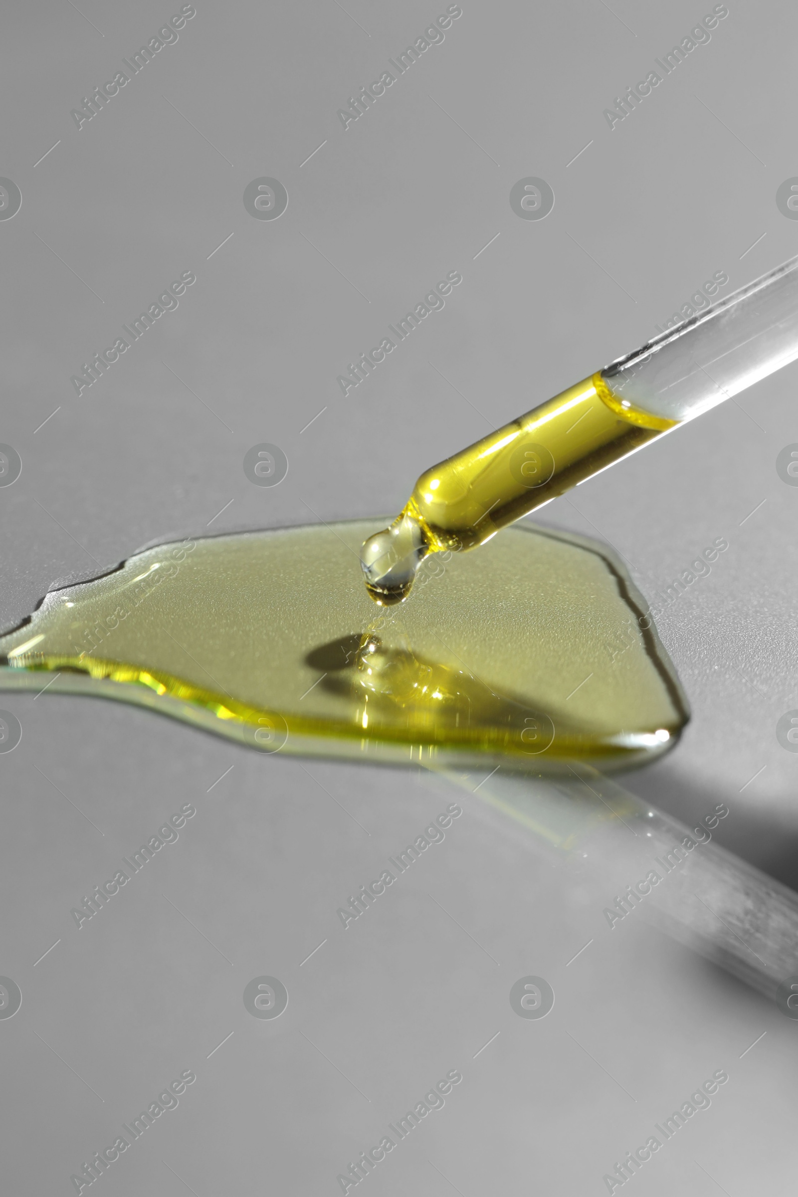 Photo of Dripping essential oil from pipette on grey background, closeup