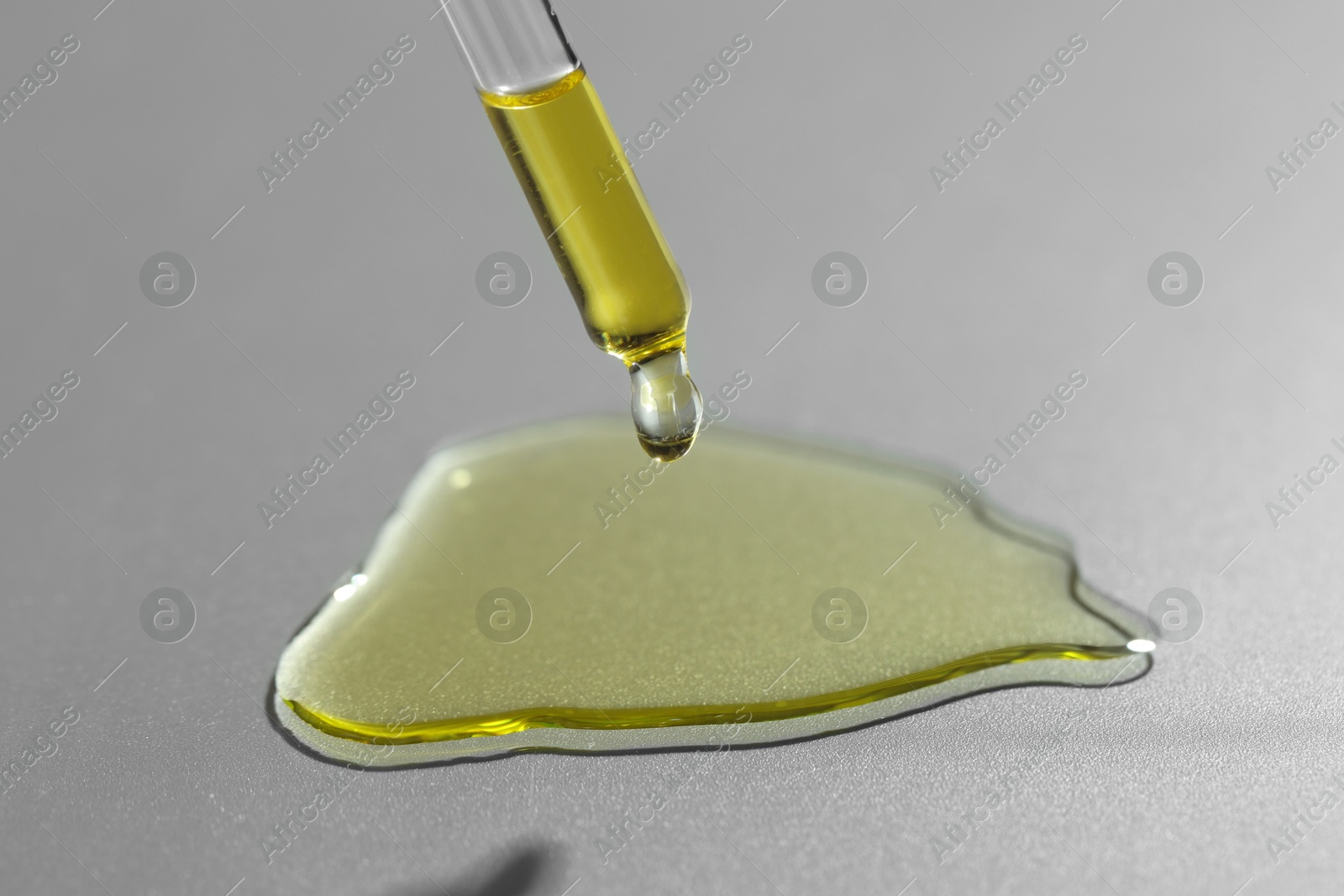 Photo of Dripping essential oil from pipette on grey background, closeup