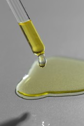 Photo of Dripping essential oil from pipette on grey background, closeup