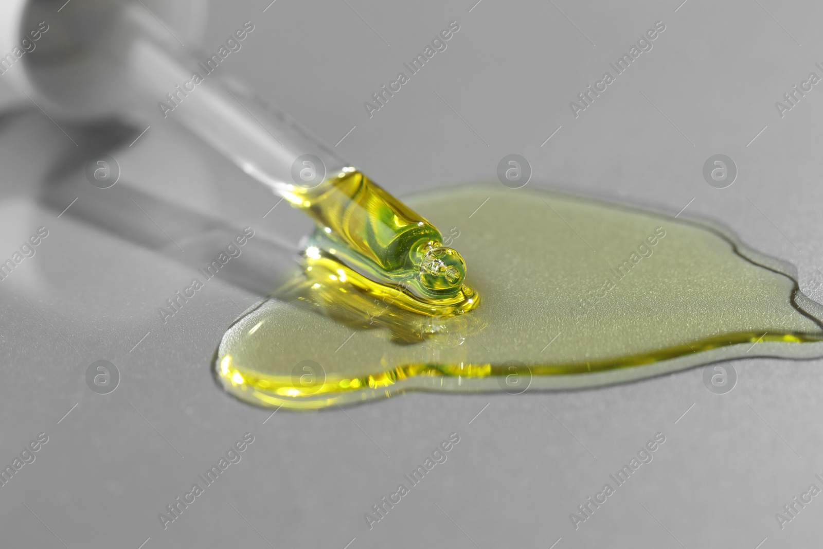 Photo of Dripping essential oil from pipette on grey background, closeup