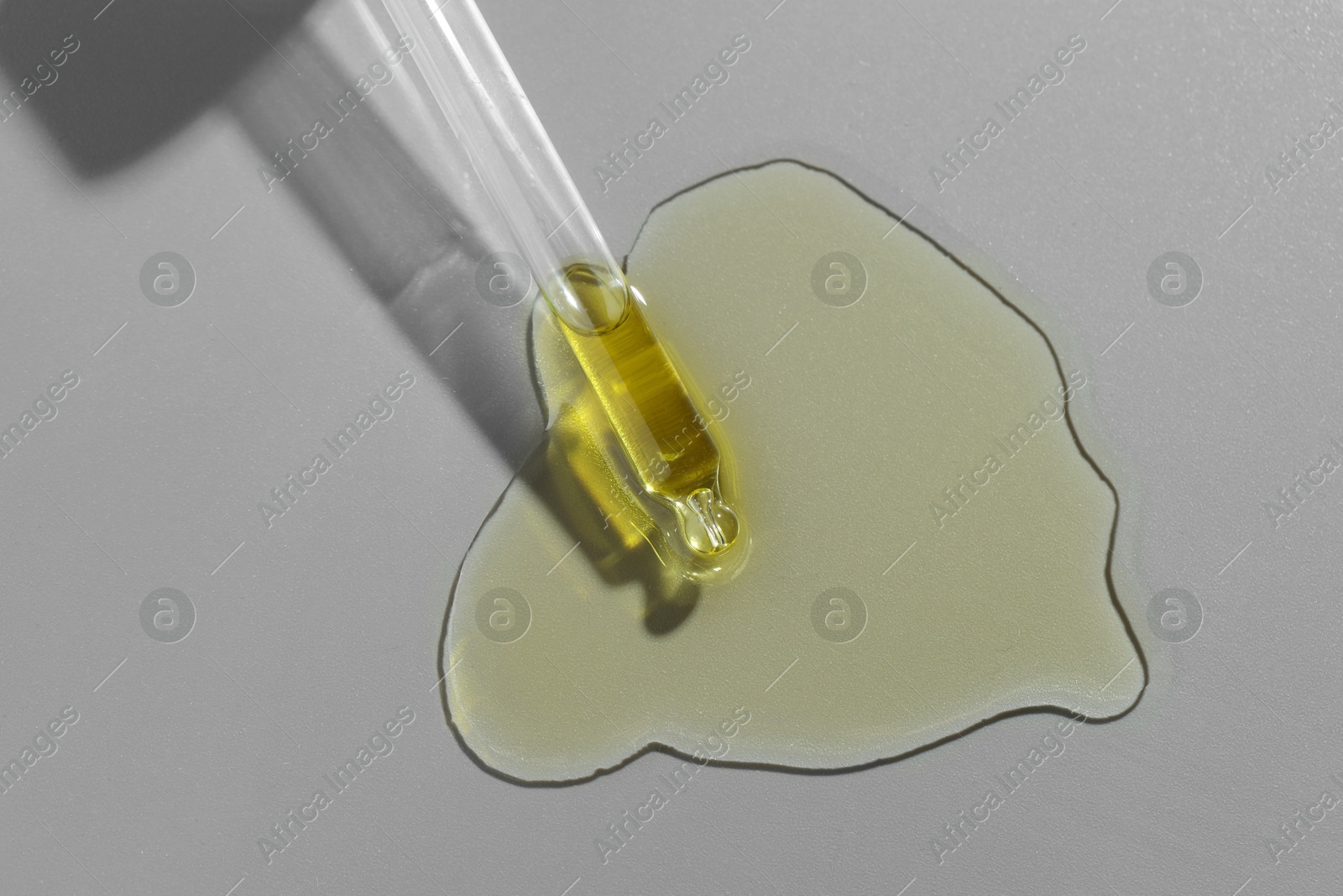 Photo of Dripping essential oil from pipette on grey background, top view