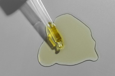 Dripping essential oil from pipette on grey background, top view