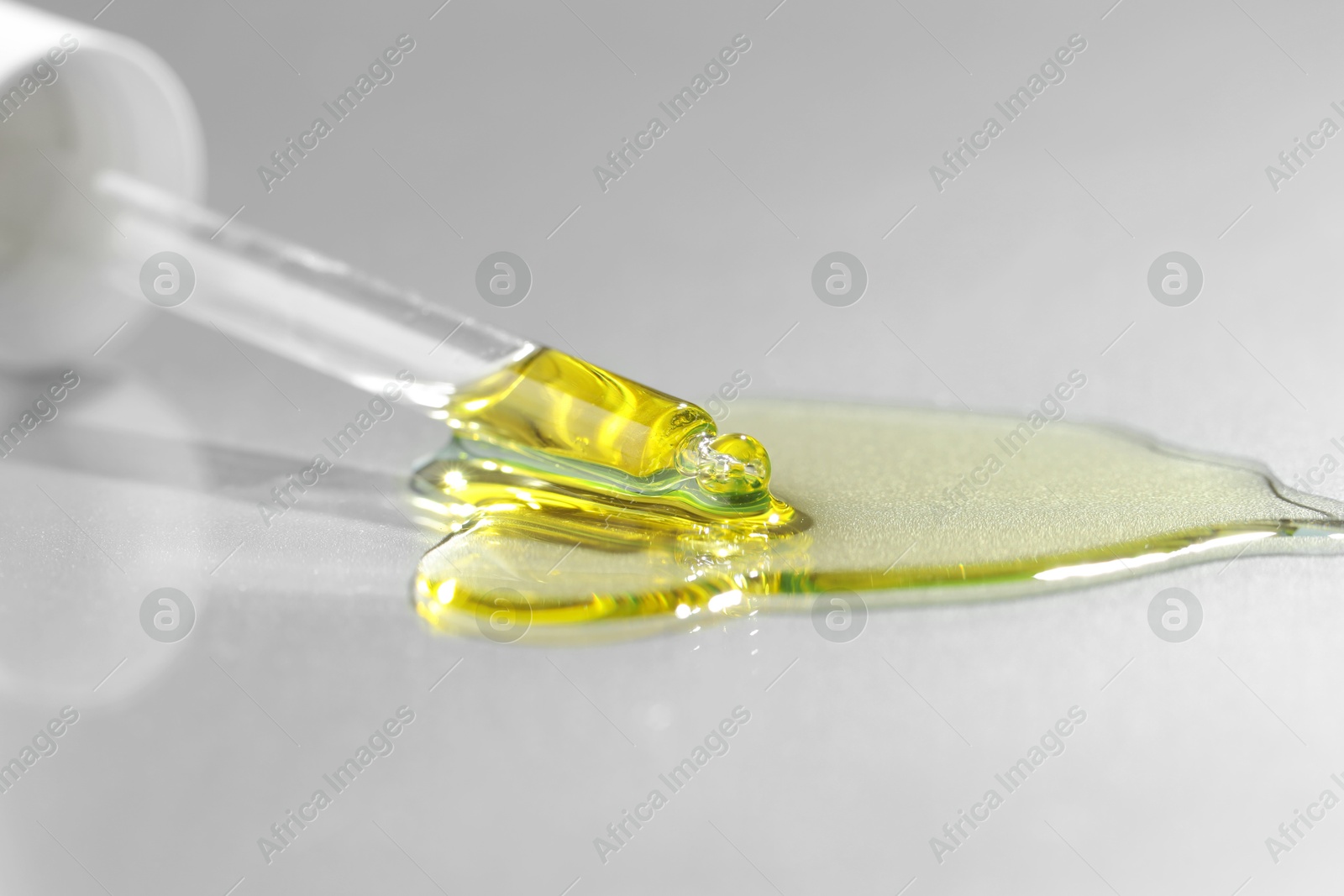 Photo of Dripping essential oil from pipette on grey background, closeup