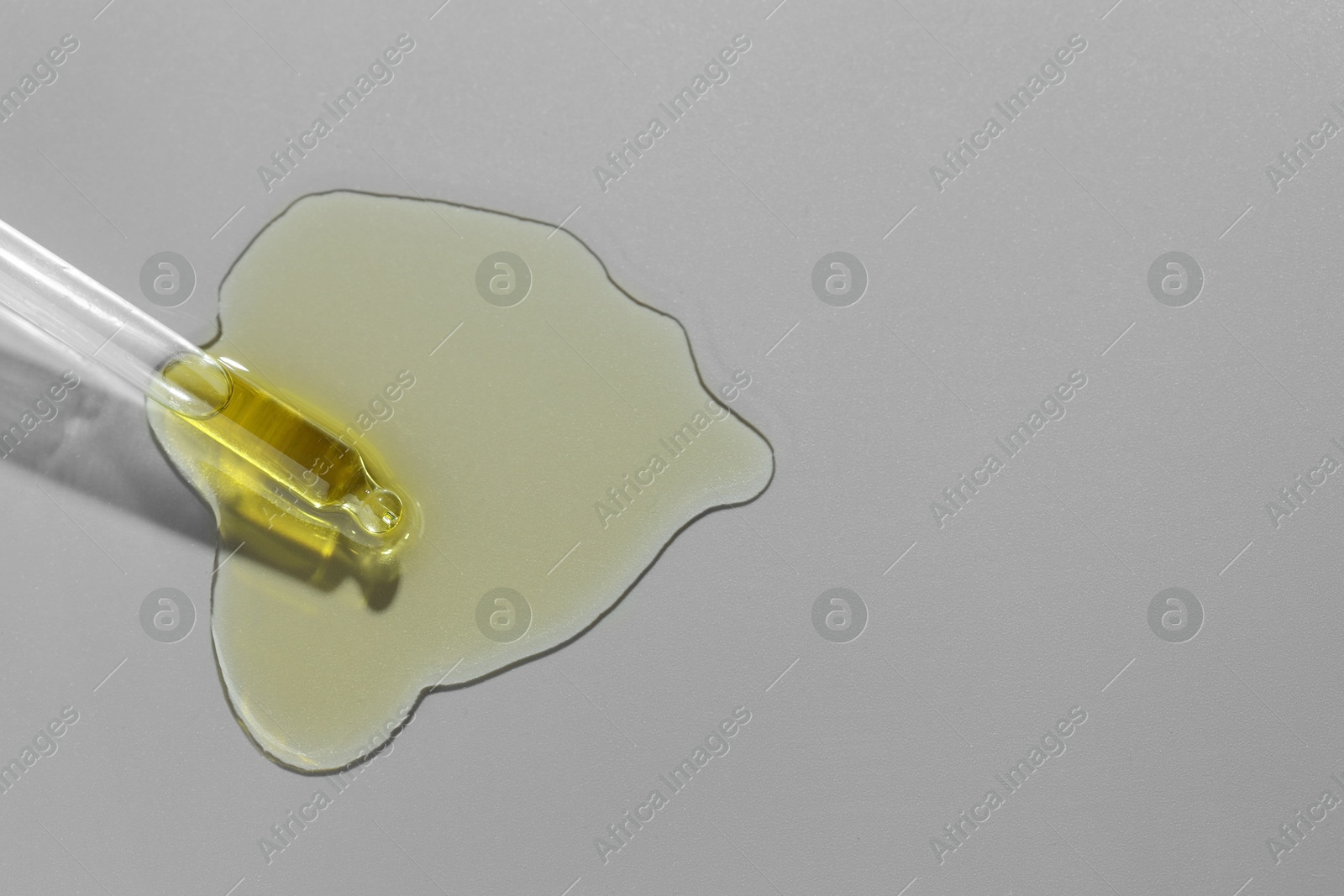 Photo of Dripping essential oil from pipette on grey background, top view. Space for text