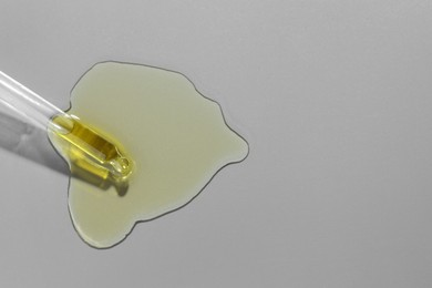 Photo of Dripping essential oil from pipette on grey background, top view. Space for text