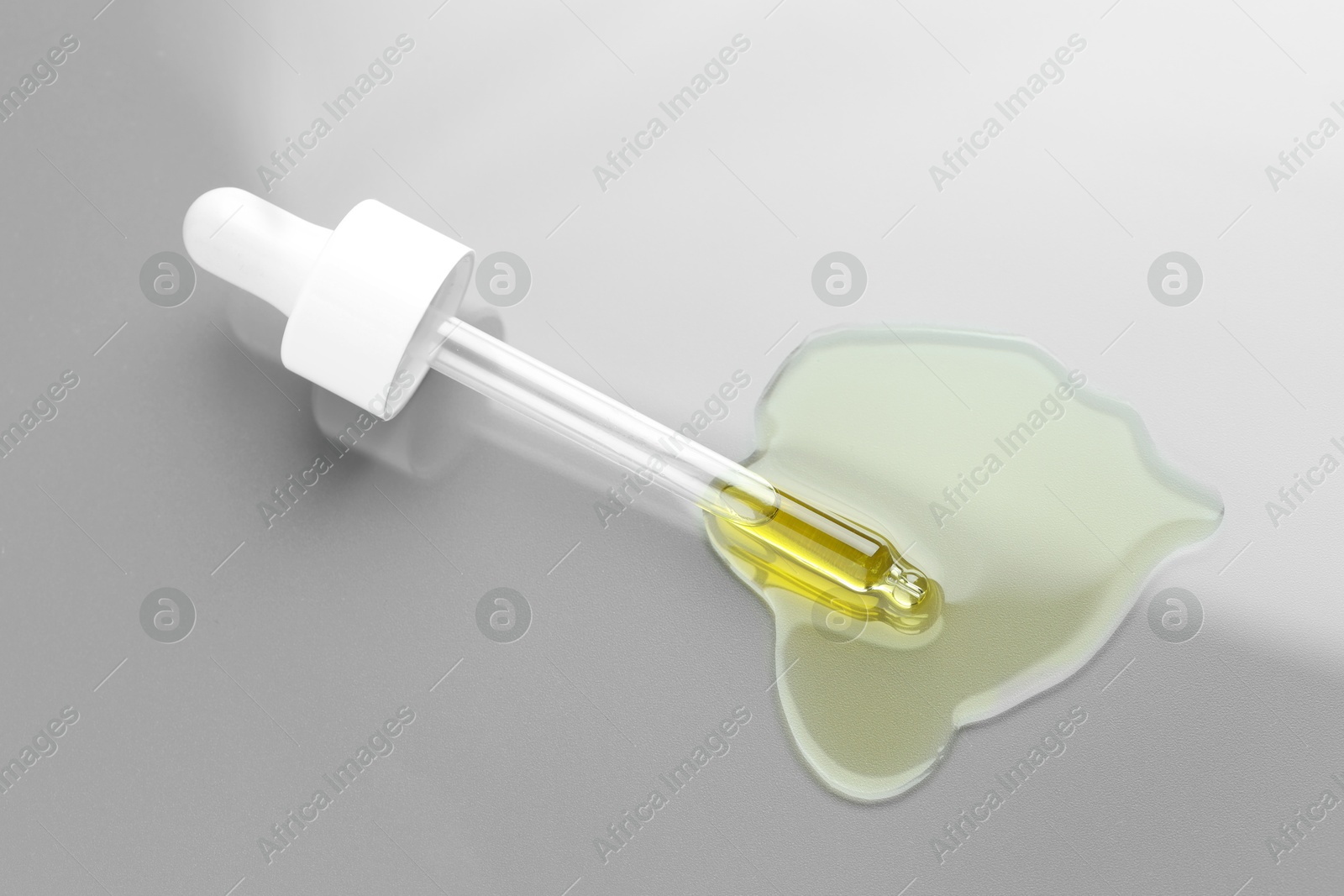 Photo of Dripping essential oil from pipette on light grey background, above view