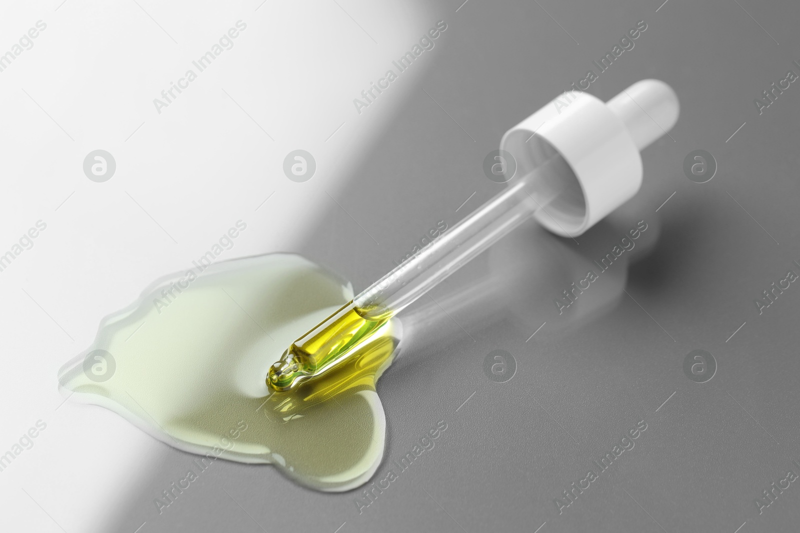 Photo of Dripping essential oil from pipette on light grey background