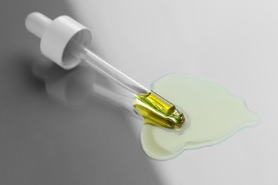 Photo of Dripping essential oil from pipette on light grey background