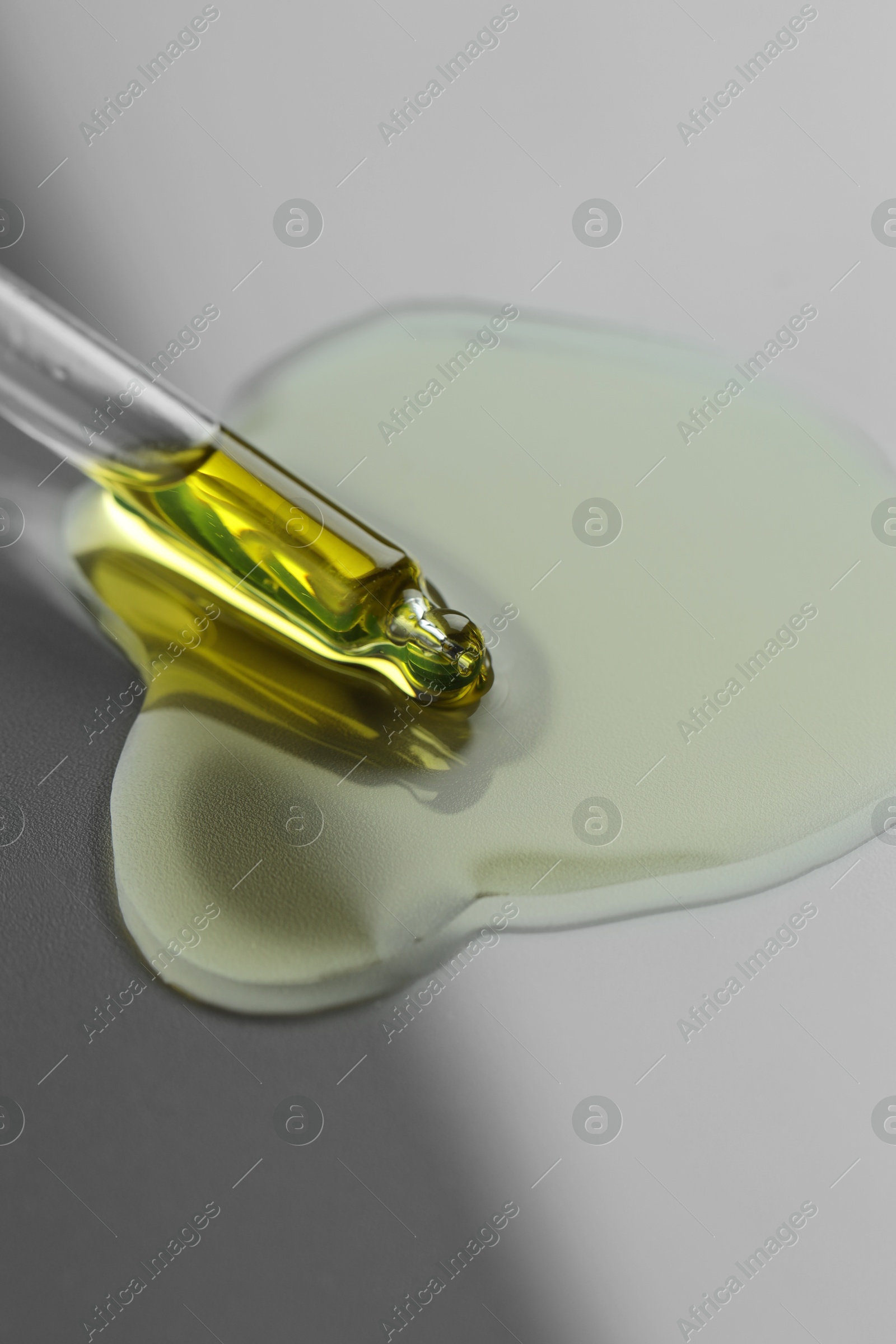 Photo of Dripping essential oil from pipette on grey background, closeup