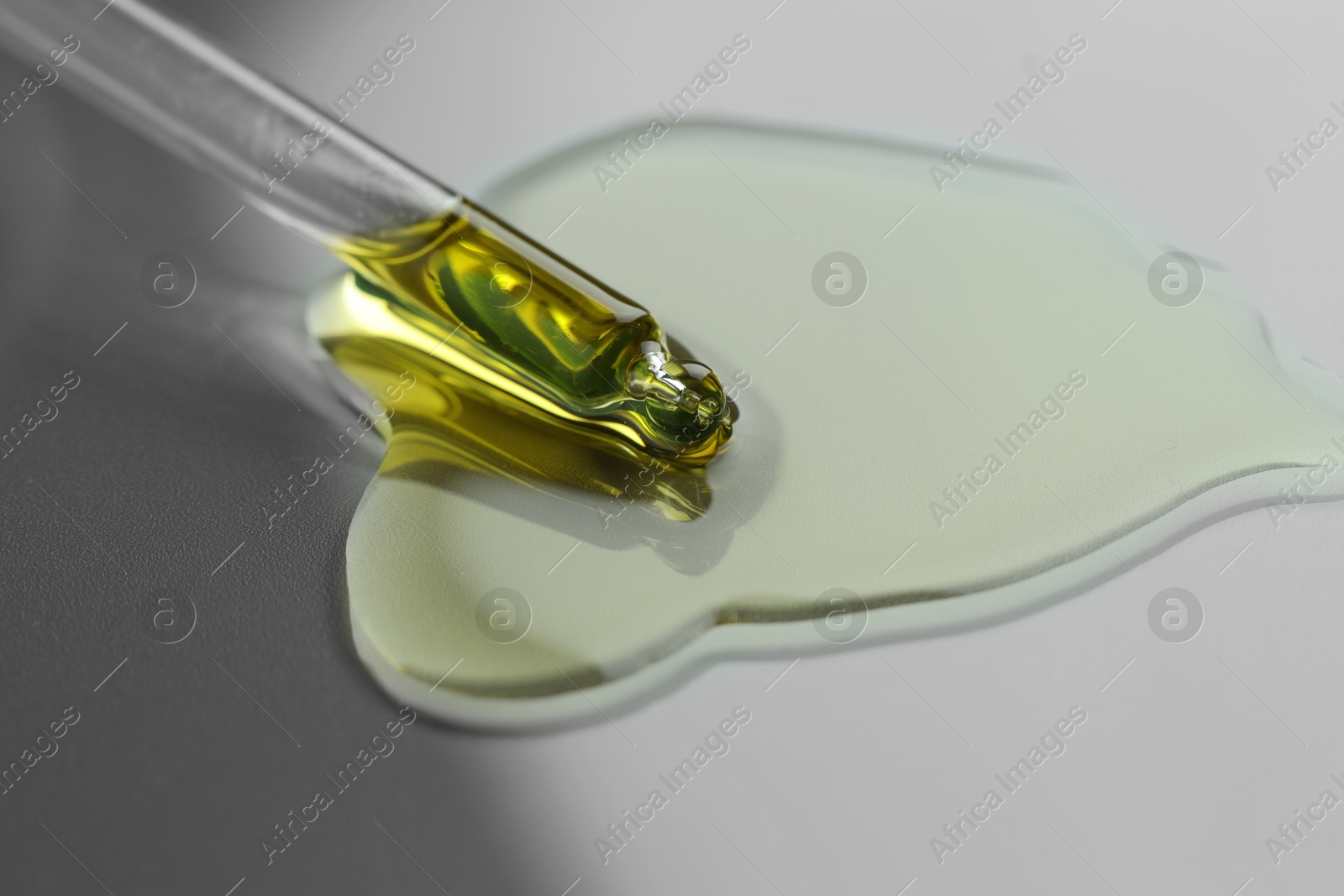 Photo of Dripping essential oil from pipette on grey background, closeup