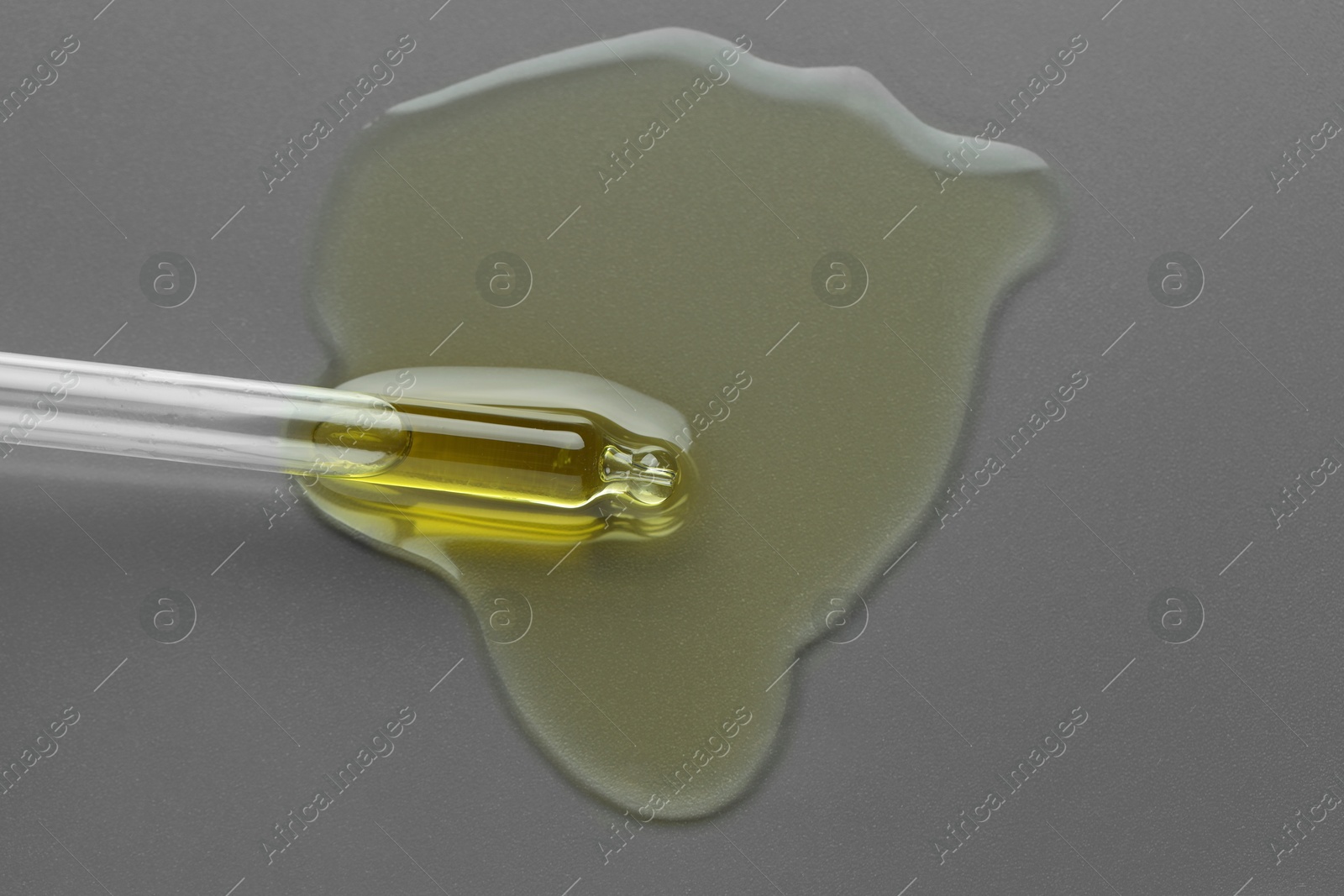 Photo of Dripping essential oil from pipette on grey background, top view