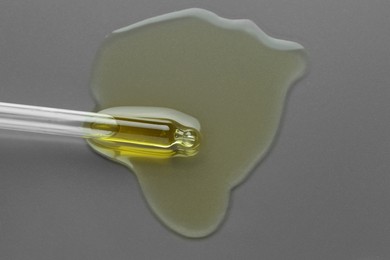 Photo of Dripping essential oil from pipette on grey background, top view