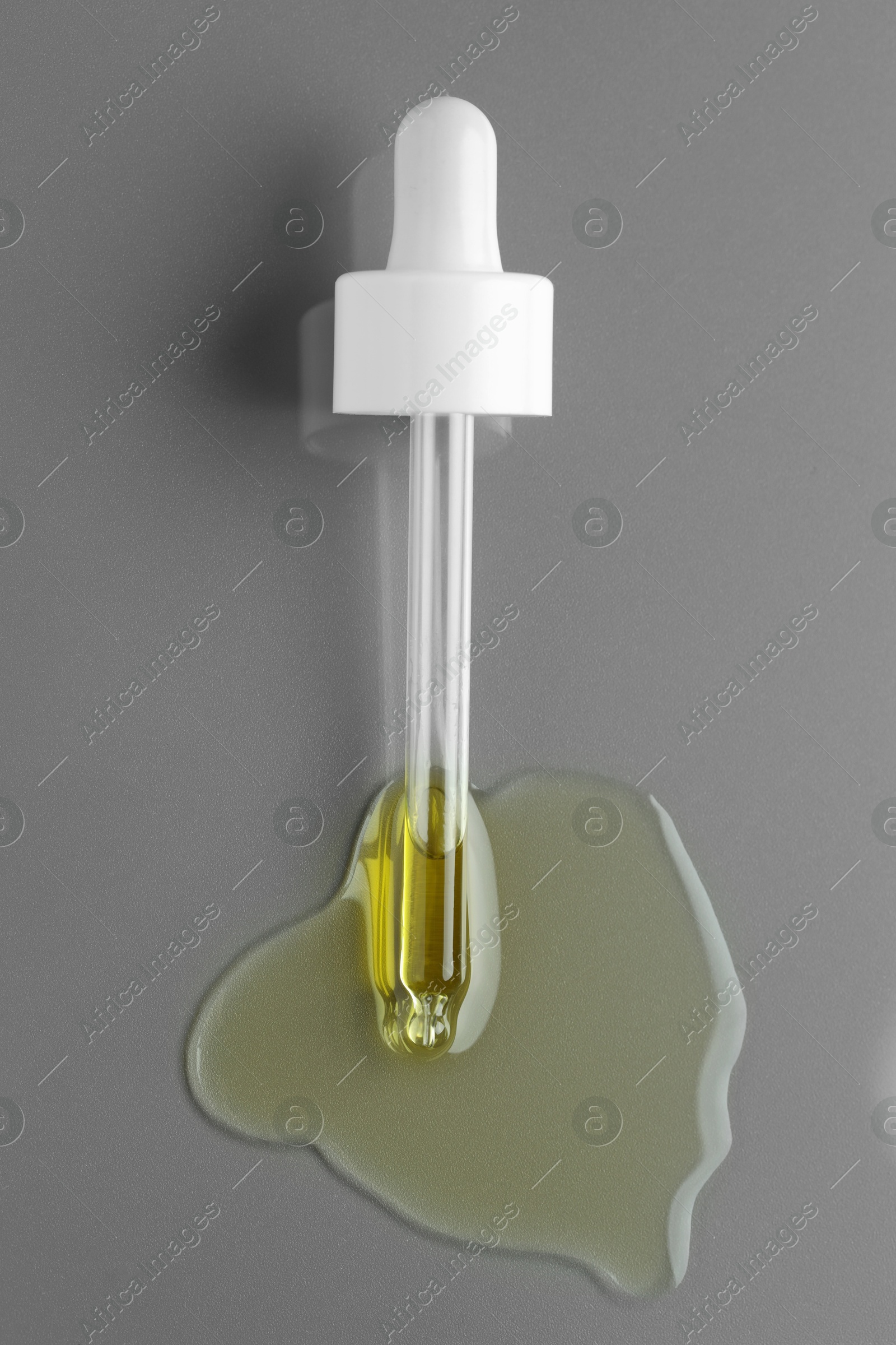 Photo of Dripping essential oil from pipette on grey background, top view