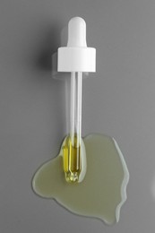 Dripping essential oil from pipette on grey background, top view