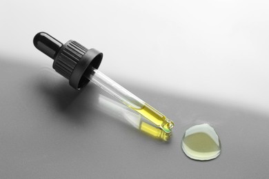 Photo of Dripping essential oil from pipette on grey background