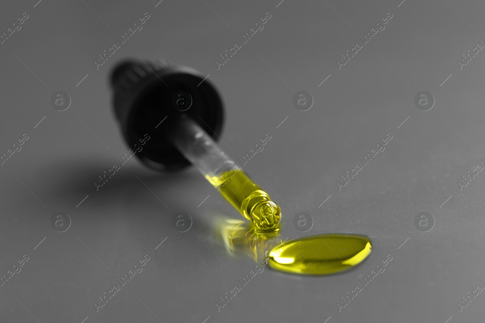 Photo of Dripping essential oil from pipette on grey background, closeup