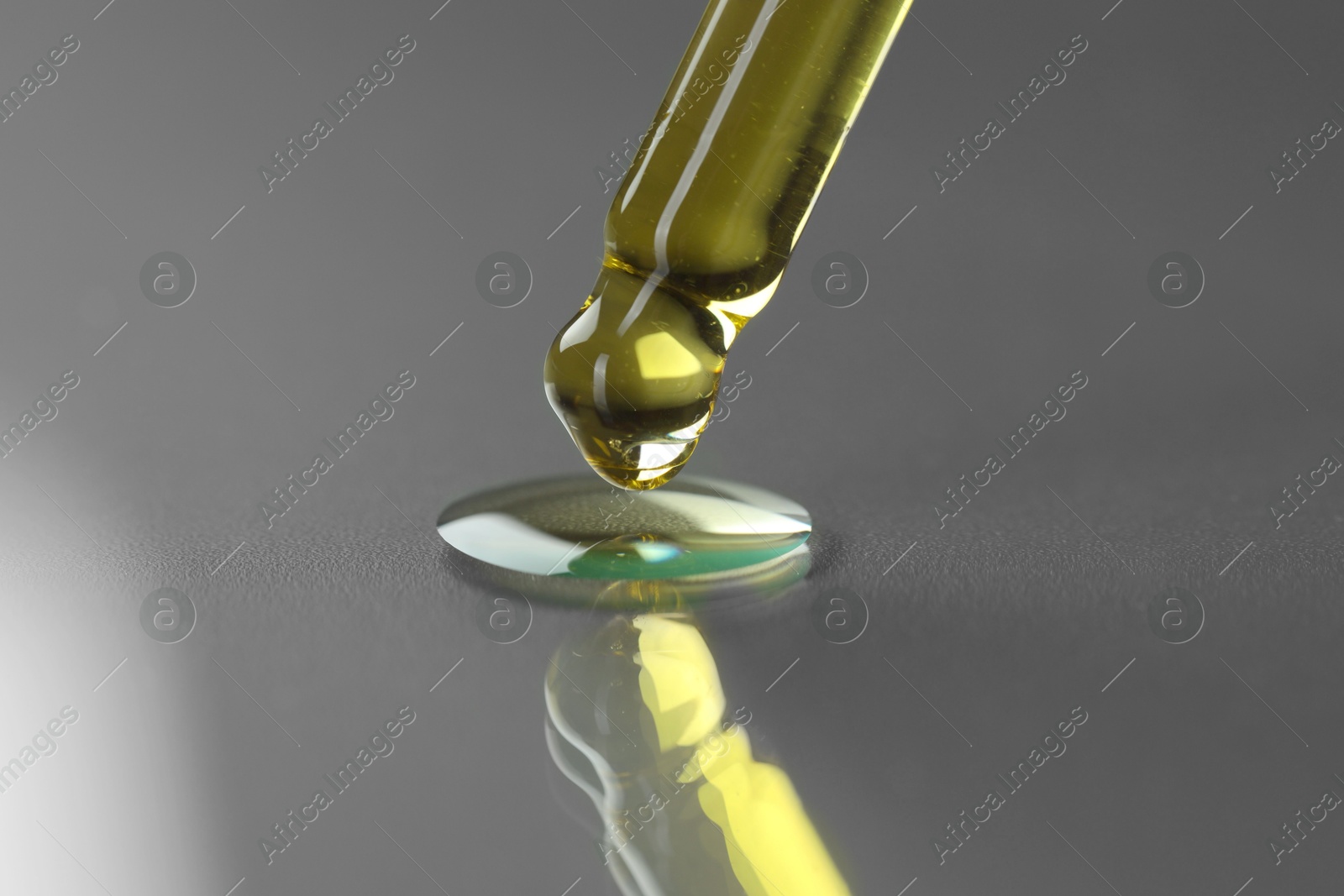 Photo of Dripping essential oil from pipette on grey background, closeup