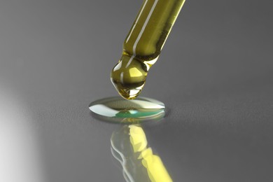 Photo of Dripping essential oil from pipette on grey background, closeup