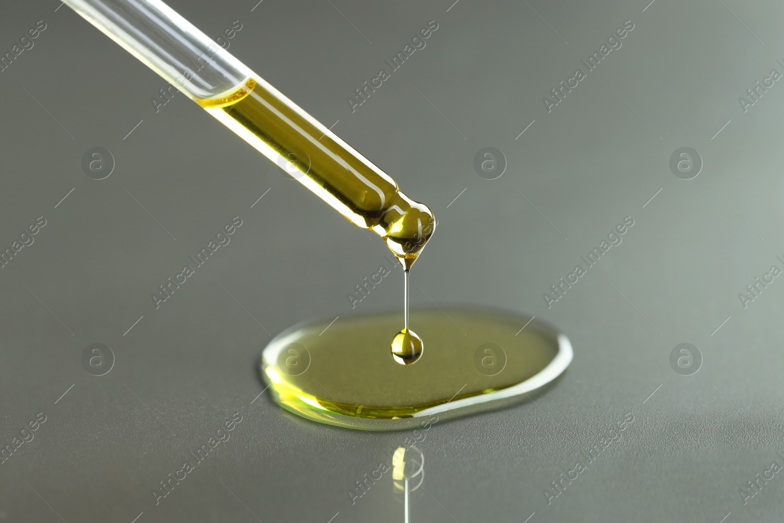 Photo of Dripping essential oil from pipette on grey background, closeup