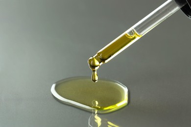 Photo of Dripping essential oil from pipette on grey background, closeup