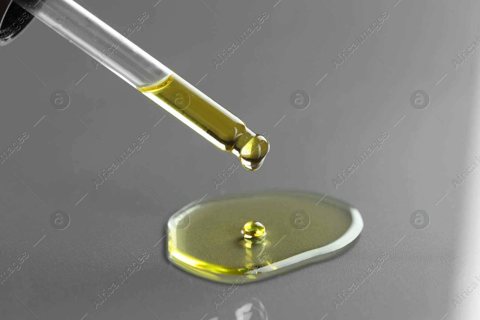 Photo of Dripping essential oil from pipette on grey background, closeup