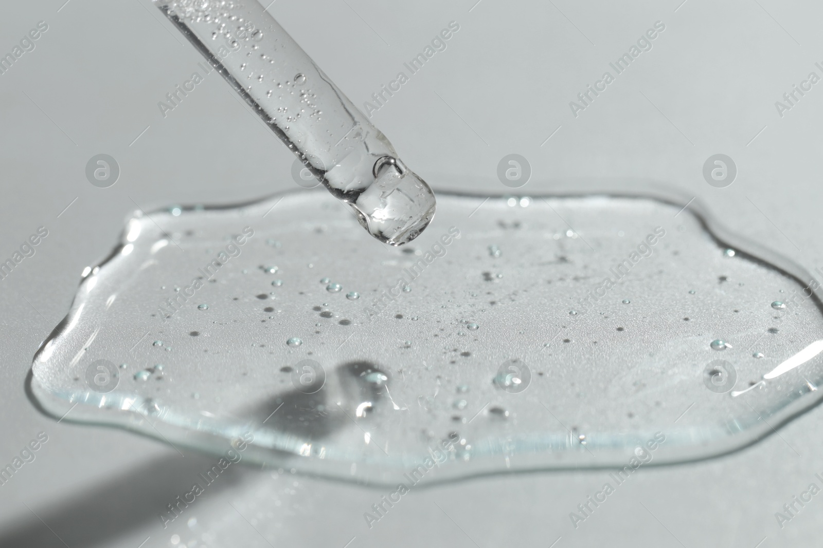 Photo of Dripping cosmetic serum from pipette on light background, closeup