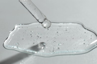 Dripping cosmetic serum from pipette on light background, closeup