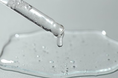 Dripping cosmetic serum from pipette on light background, closeup