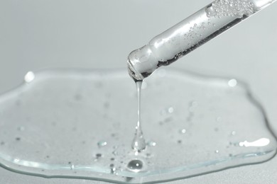 Photo of Dripping cosmetic serum from pipette on light background, closeup