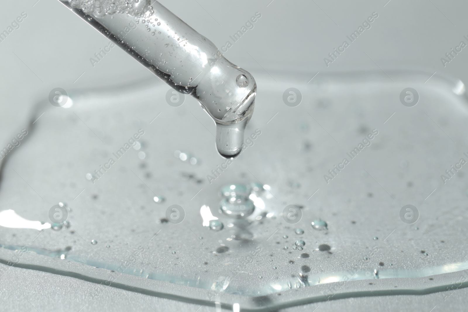 Photo of Dripping cosmetic serum from pipette on light background, closeup